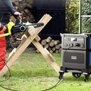 Person using a chainsaw with a portable generator in an outdoor setting