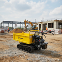 A yellow compact dump truck with tracked wheels and a small engine on a construction site, with an excavator and building structure in the background.