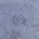 A close-up of a scratched, used clear plastic or acrylic drain cover set into a scratched, gray metal surface.