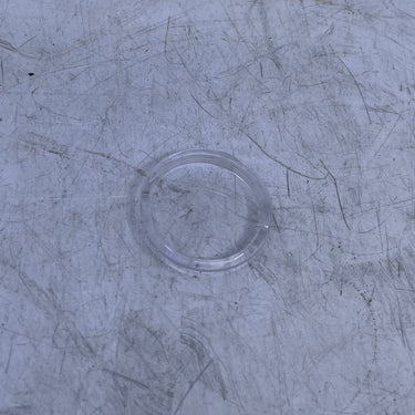 A close-up of a scratched, used clear plastic or acrylic drain cover set into a scratched, gray metal surface.