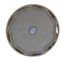 A circular beige plastic cap or cover with a central hole, photographed from above on a scratched light gray surface.