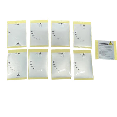 Eight small white rectangular items with printed diagrams are arranged on a dark gray carpet next to a cardboard shipping box, with the bottom of a person's shoes visible at the edge.