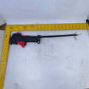 A black and red mechanical tool with a long thin rod is laid on a white lightbox background, alongside a yellow L-square measuring ruler to show its dimensions.