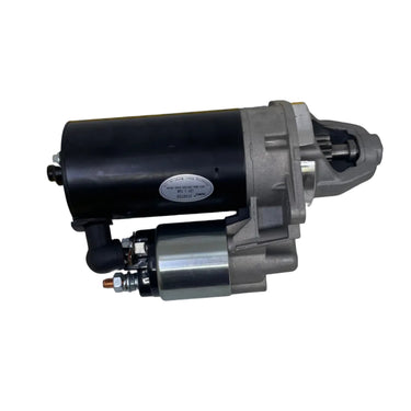 A used automotive starter motor shown on a white surface, positioned next to a yellow L-shaped tape measure to indicate its size.