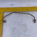 A curved metal automotive part with two threaded ends, shown on a scratched white surface with a yellow L-square ruler for scale.