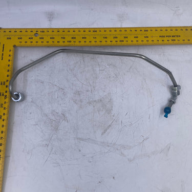A curved metal automotive hose with a blue fitting and silver clamp, displayed on a scratched white surface next to a yellow L-square ruler for scale.