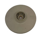 A beige plastic circular component with a central hub, photographed on a scratched light gray surface.