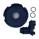 A black circular plastic housing component with a central metal ring, shown alongside a black plastic mechanical fitting and two small black O-rings on a light gray scratched surface.