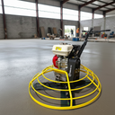 A concrete grinder with a large yellow safety cage, mounted on a black wheeled frame, shown in a large concrete warehouse floor.