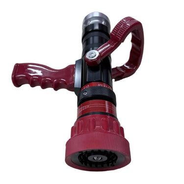 A red and black adjustable garden hose nozzle with a curved red loop handle, placed on a light wood-grain surface.